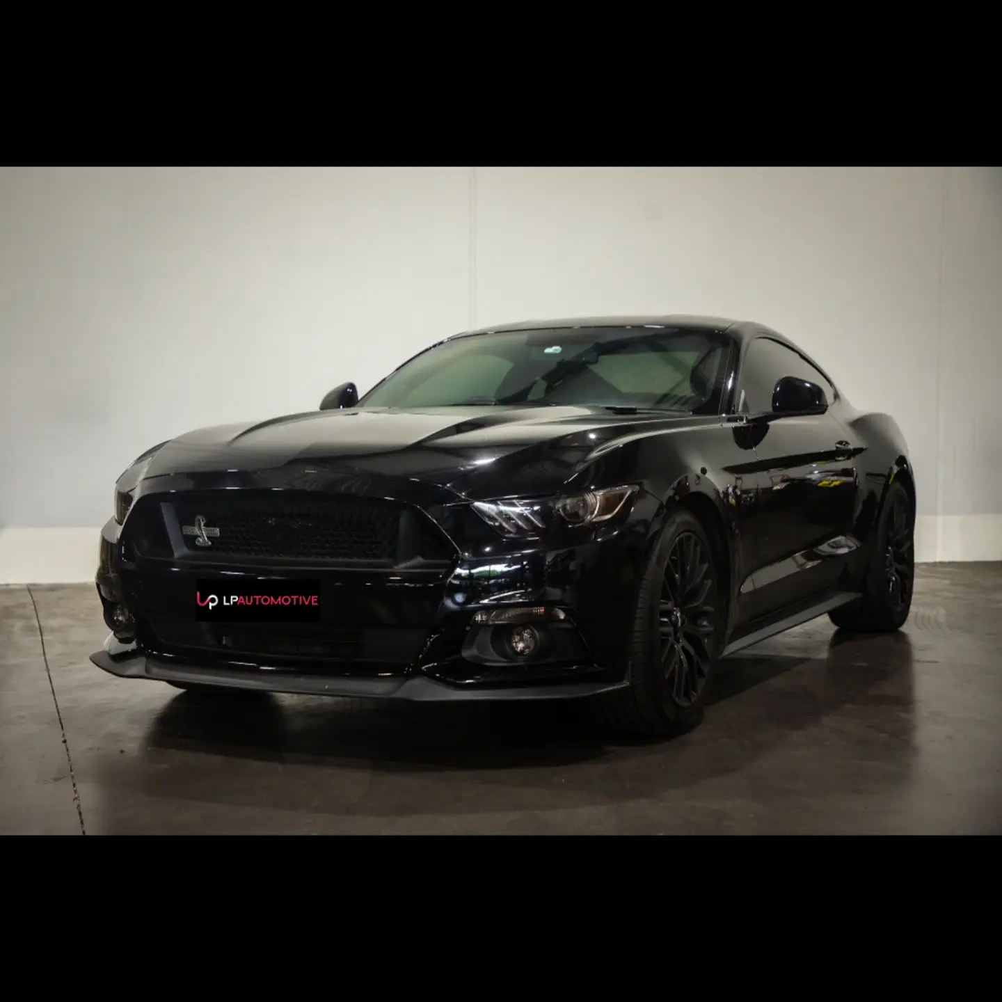 A blacked-out Ford Mustang photographed against the white wall at LP Automotive, wearing an LP Automotive dealer plate