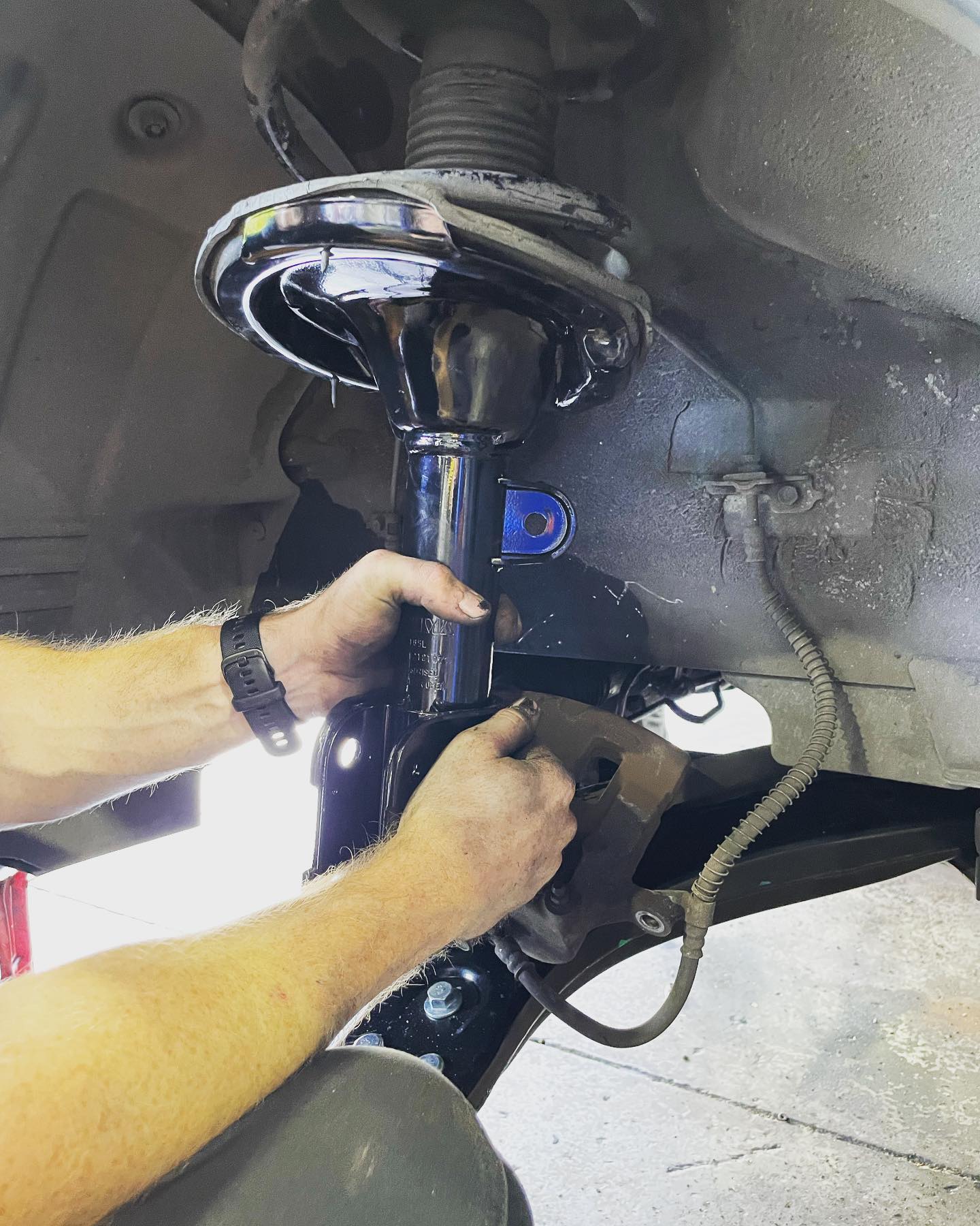 A mechanic's hands fitting a new front strut under a car on the hoist at LP Automotive